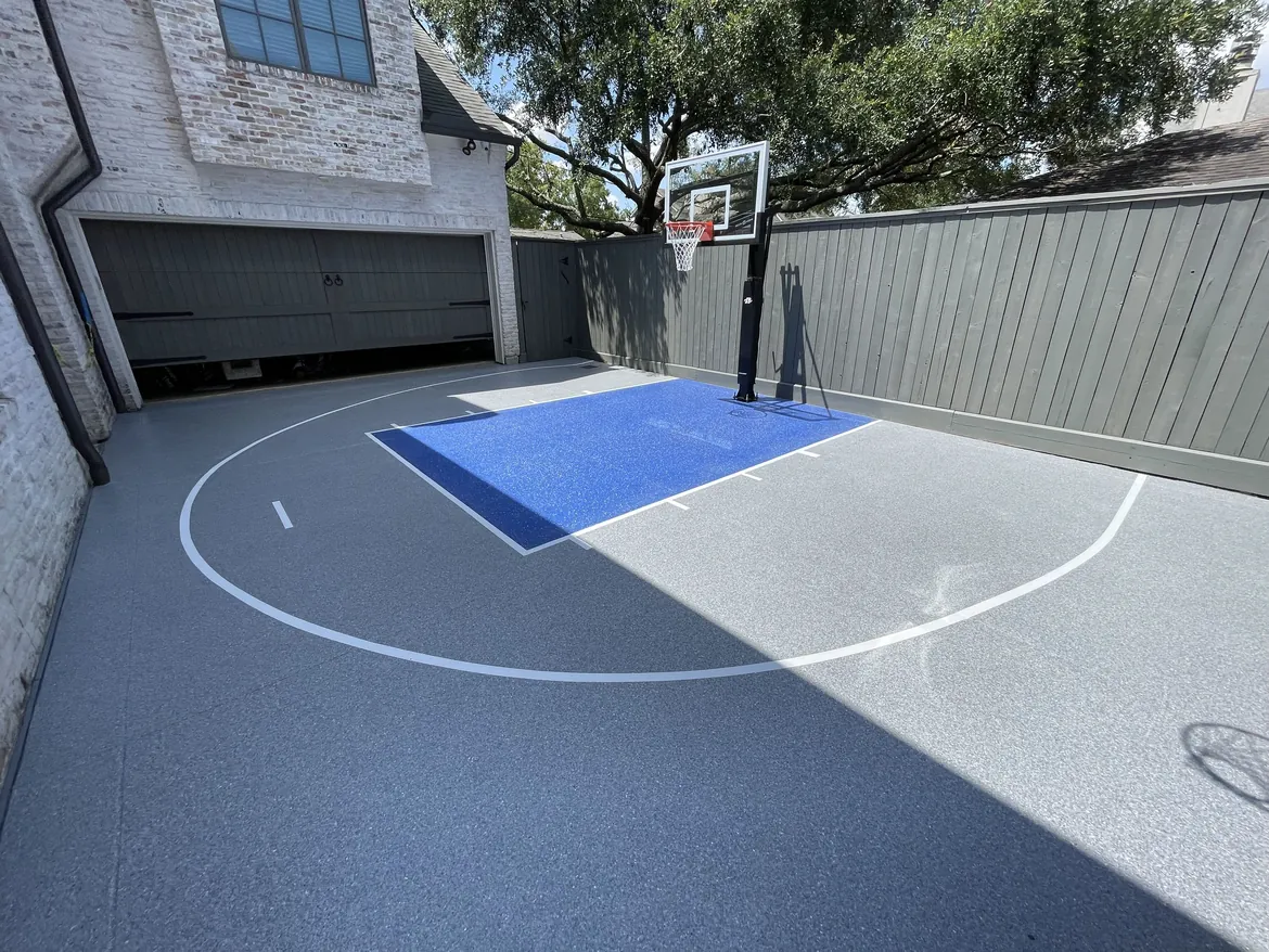 Blue and gray coating on a backyard concrete sport court beside a Houston home