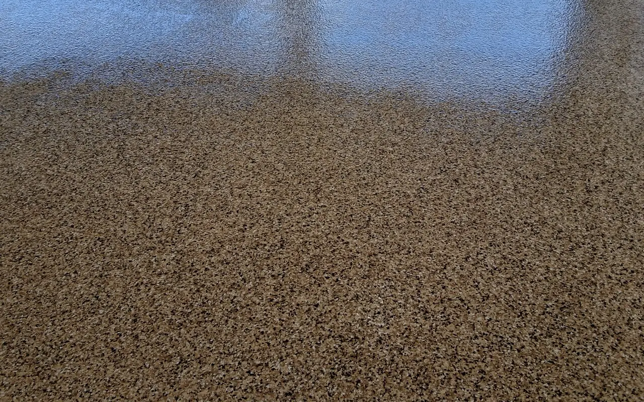 Tan flake garage floor with a glossy clear topcoat catching sunlight at the open door