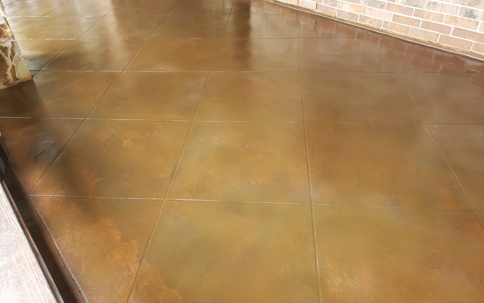 Brown acid stained concrete slab with saw cut joints beside a brick wall