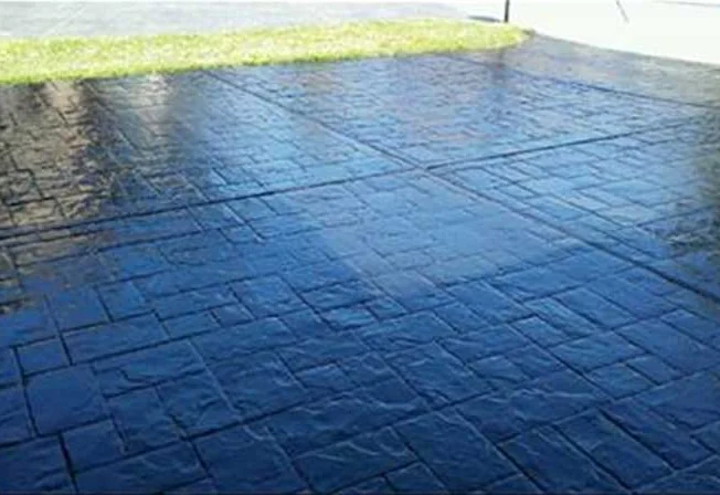 Glossy dark stained concrete driveway with a slate pattern beside a lawn
