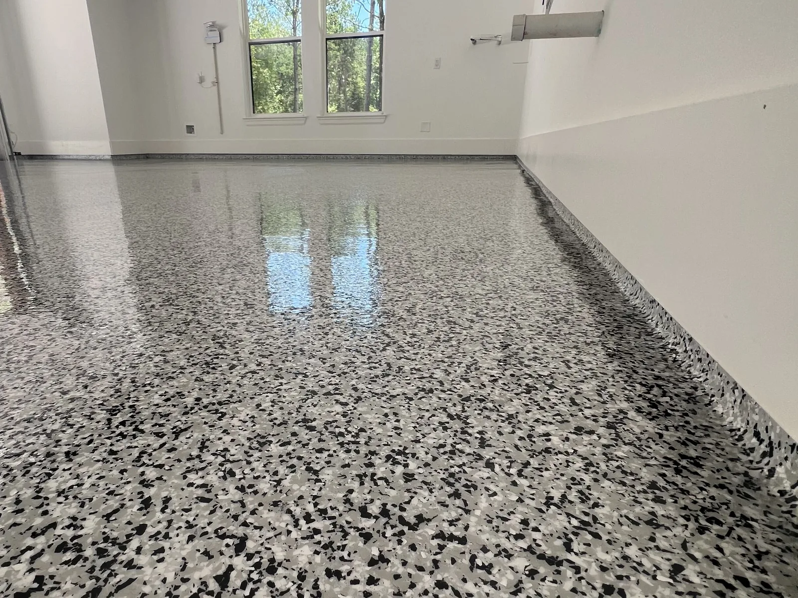 Black and white flake epoxy garage floor with a high-gloss finish and daylight from the windows