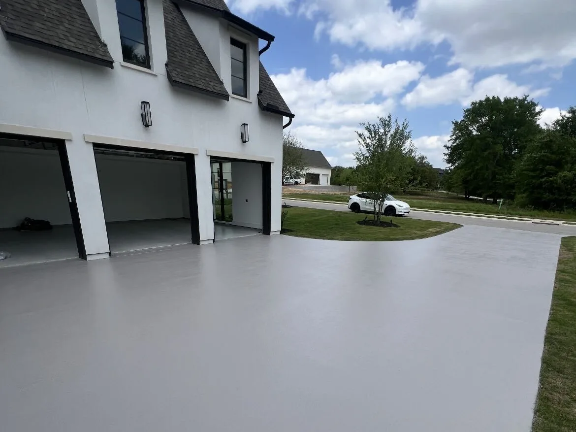 Coated gray driveway apron in front of a home with three garage doors