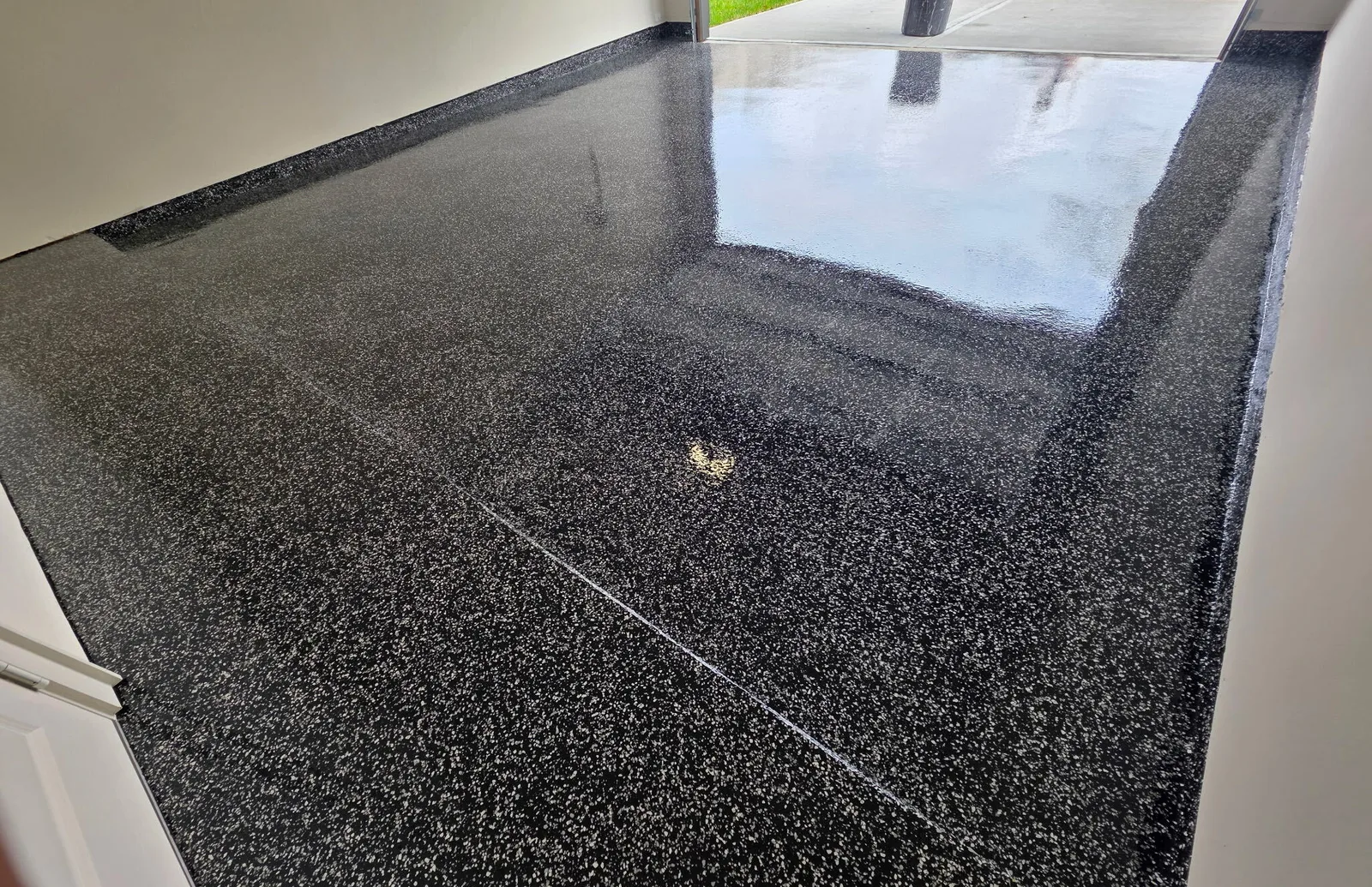 Black and white flake epoxy garage floor with the door open to the driveway