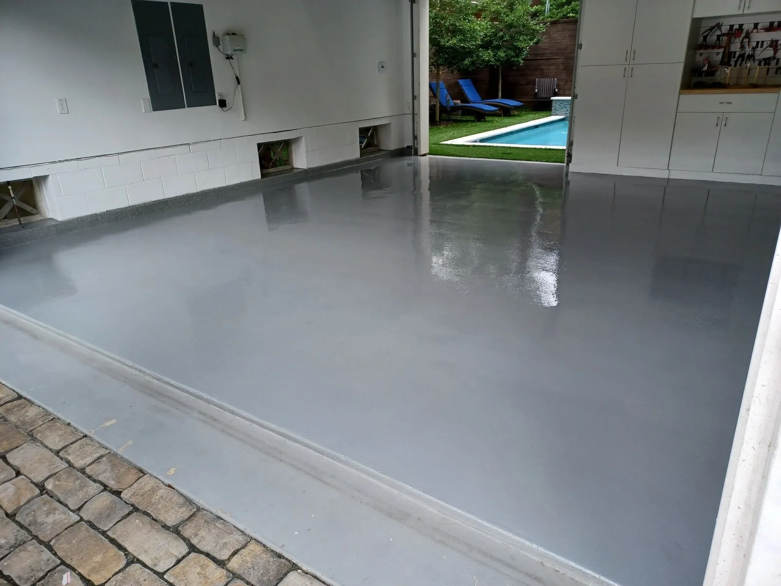 Gray solid-color garage floor coating with the door open to a backyard pool