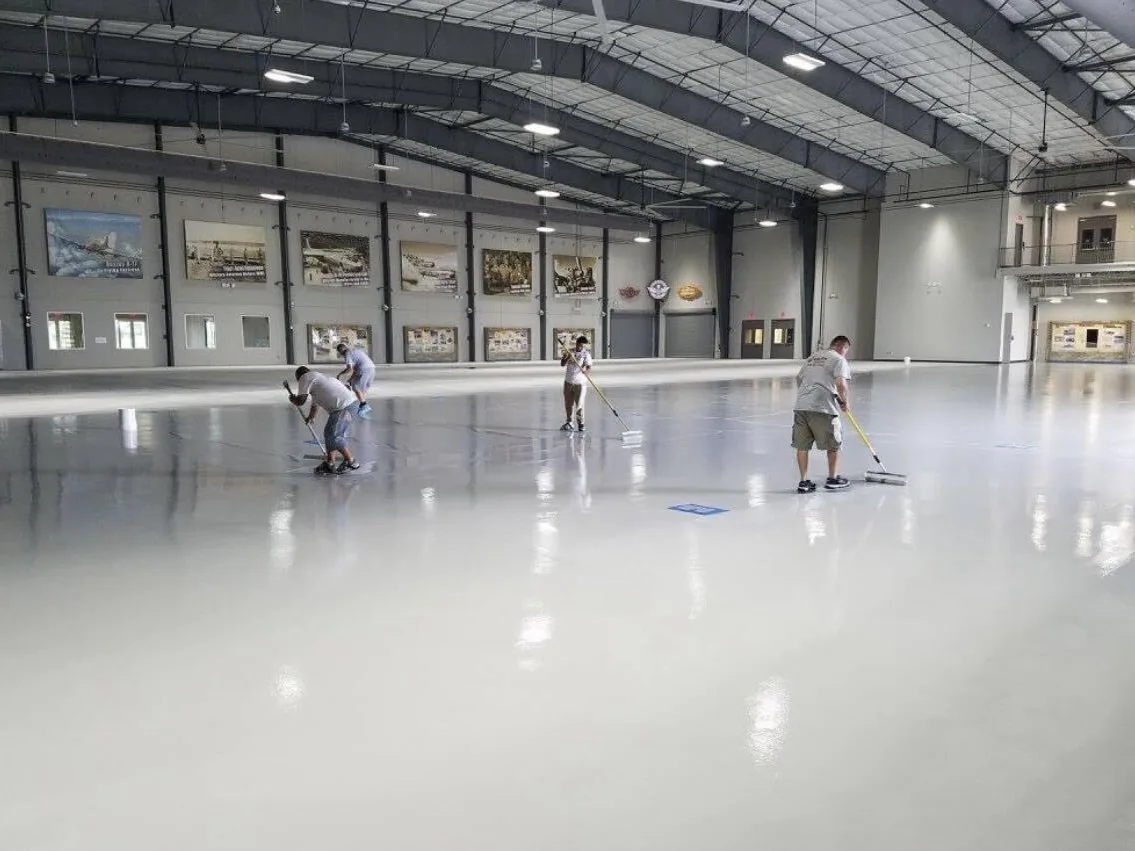 Epoxy One crew rolling a fresh white floor coating across an aircraft hangar floor