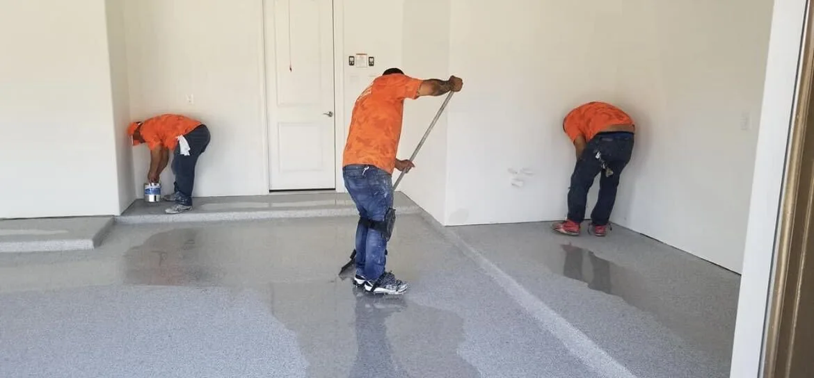 Crew rolling floor coating across a garage slab during installation