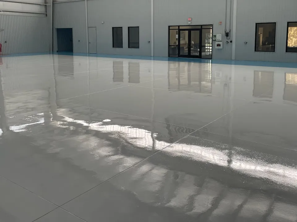 Glossy light gray coated floor across a large aircraft hangar, office doors and windows along the back wall
