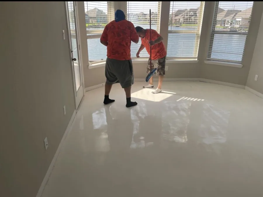 Crew finishing a white epoxy floor in a room overlooking a lake
