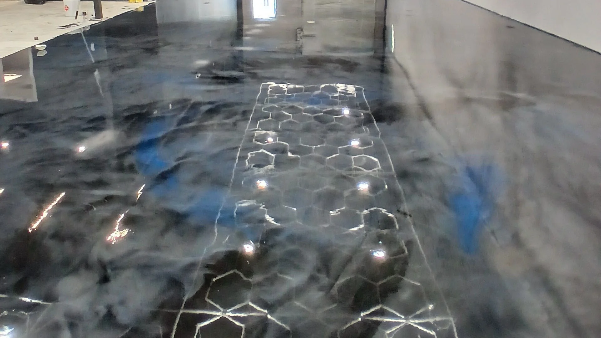 Dark metallic epoxy showroom floor reflecting hexagon ceiling lights
