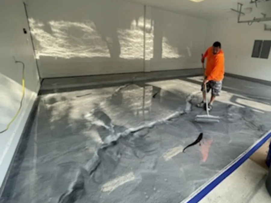 Crew member rolling a silver metallic epoxy floor in a garage