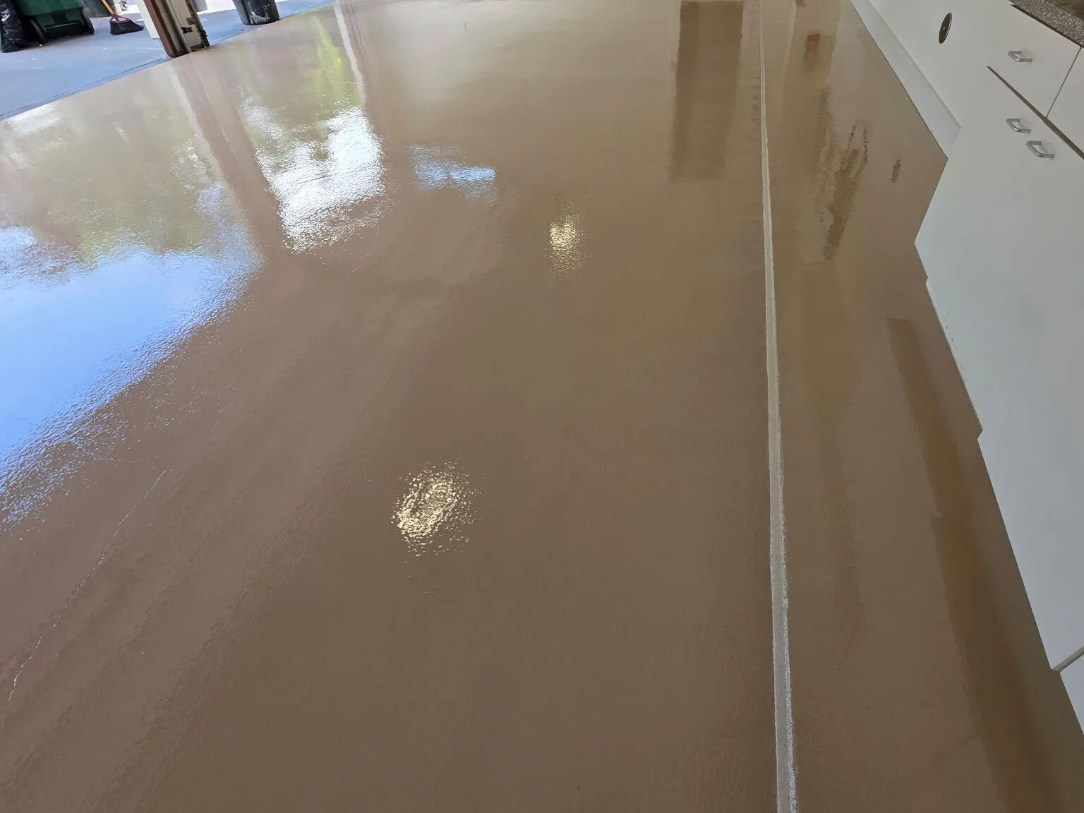 High-gloss tan polyaspartic floor coating in a Houston garage with white cabinets