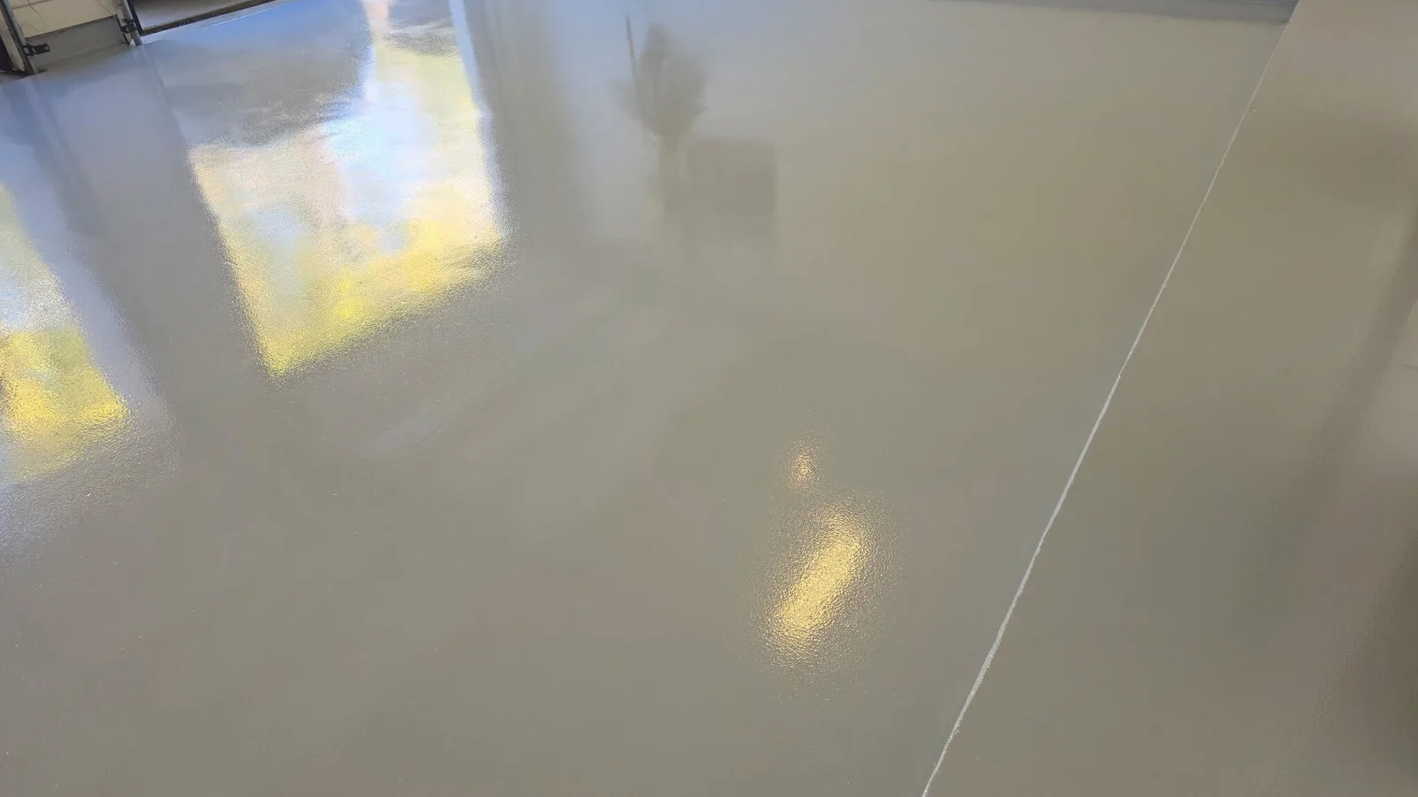 Wide high-gloss tan polyaspartic garage floor reflecting daylight from the open door