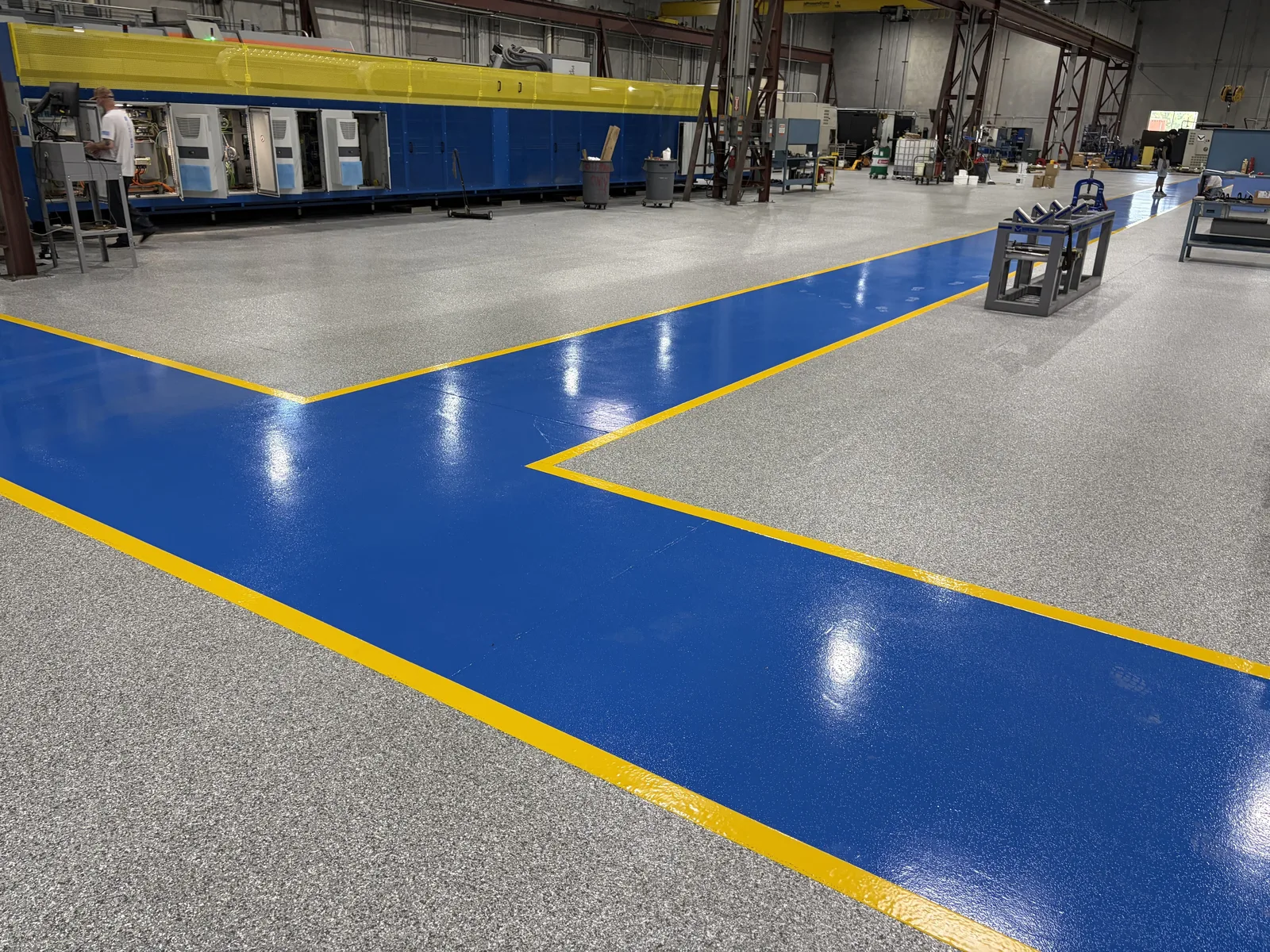 Manufacturing floor with a blue safety walkway and yellow striping over gray flake