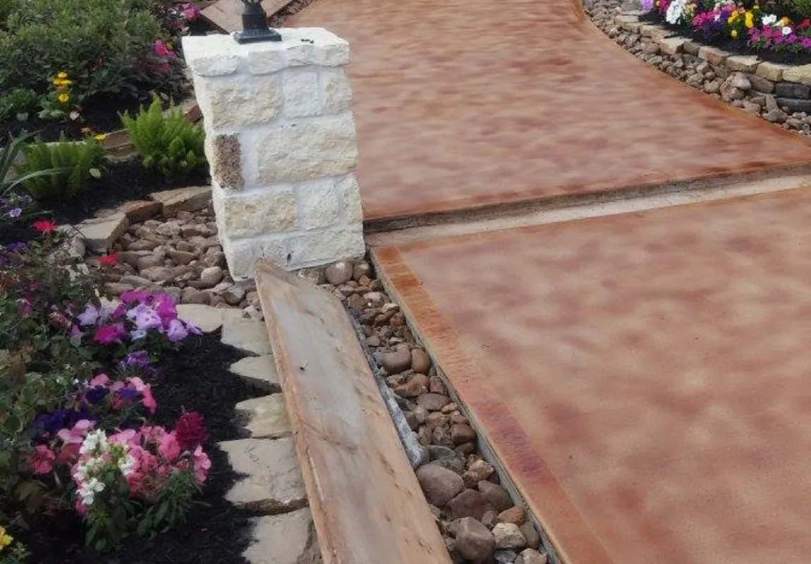 Copper acid stained front walk between stone pillars and flower beds