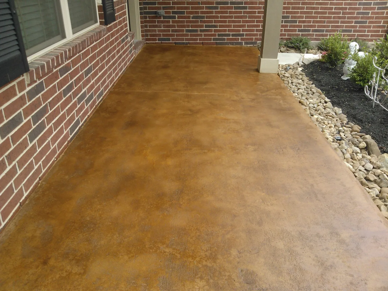 Copper stained concrete front porch alongside a brick wall
