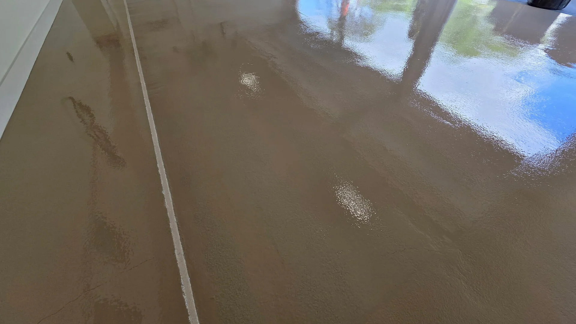Wide tan high-gloss garage floor coating reflecting daylight from the open door
