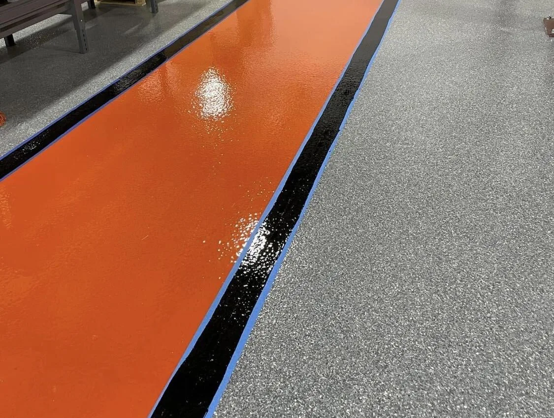 Orange safety walkway coating with a black and blue border beside a gray flake floor