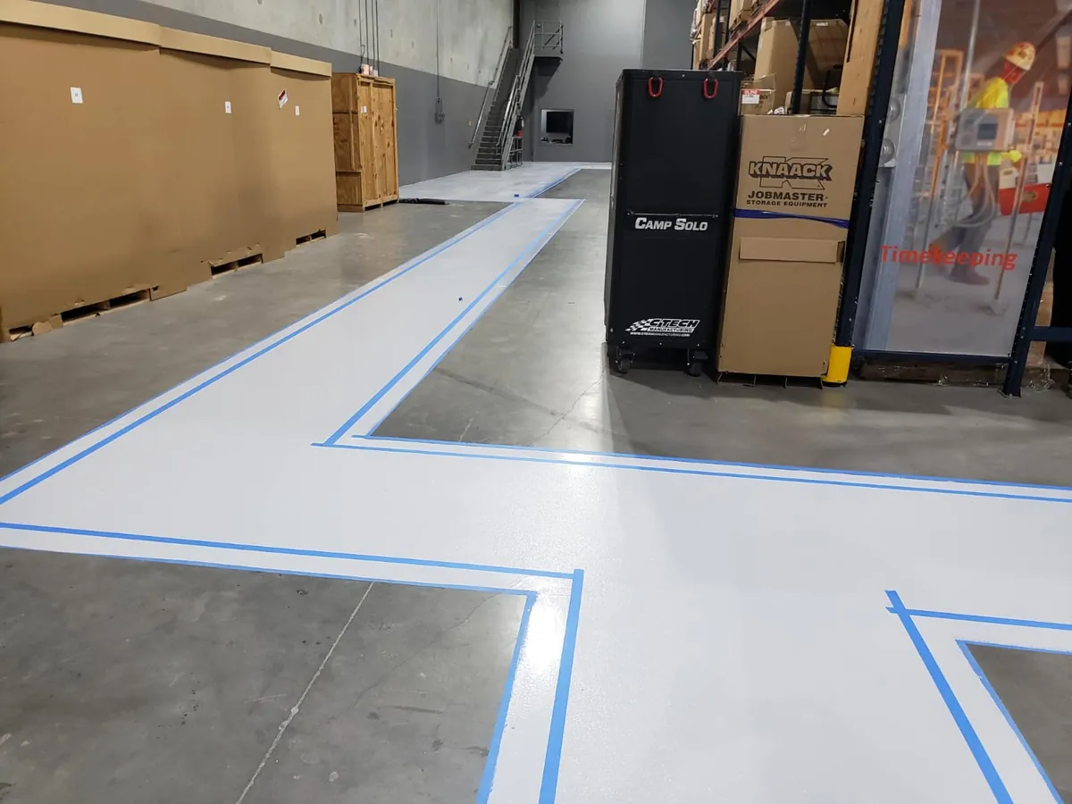 Light gray polyaspartic walkway with blue edge lines beside the racking