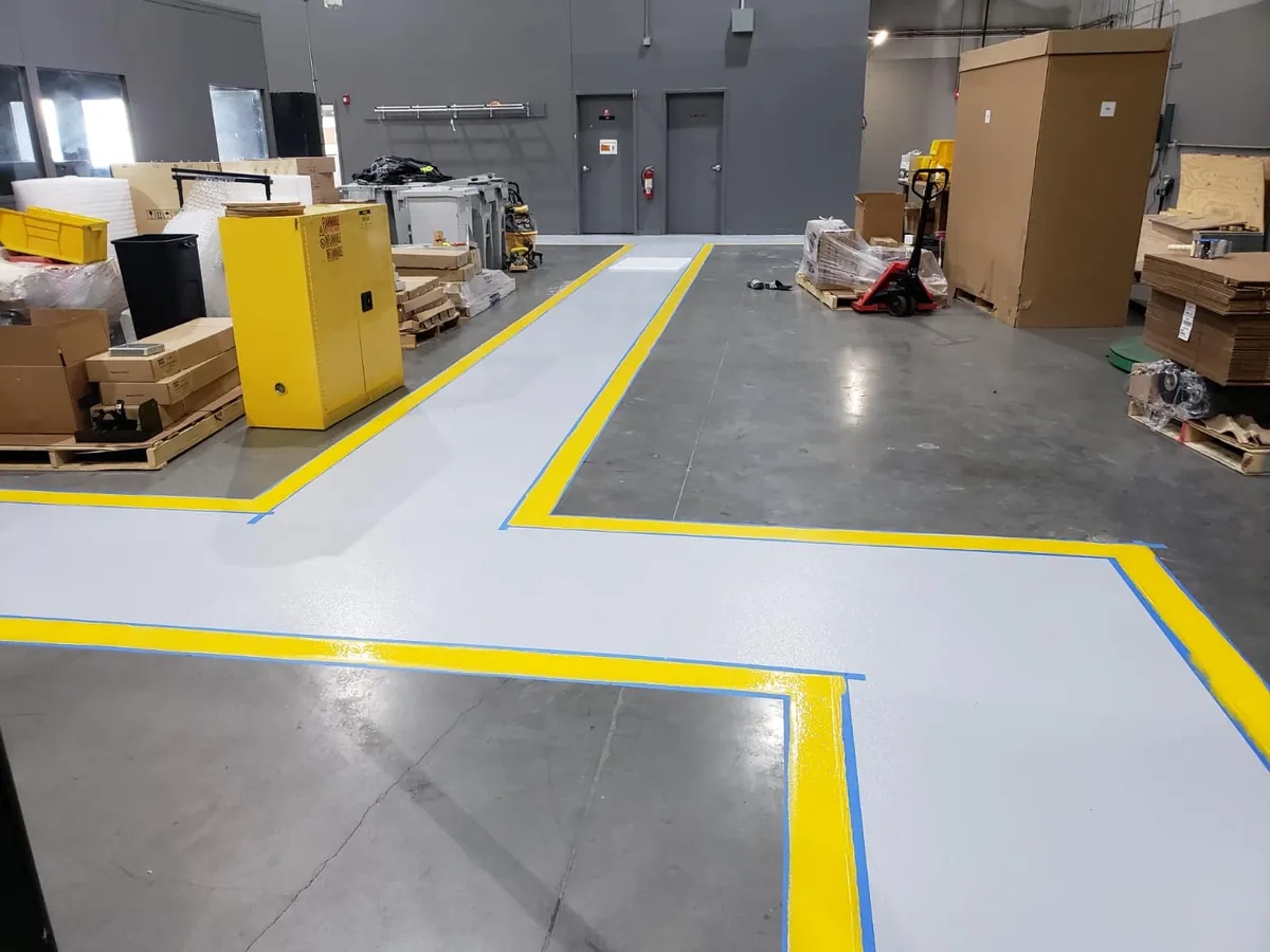 Gray walkway coating with a yellow safety border beside pallet racking