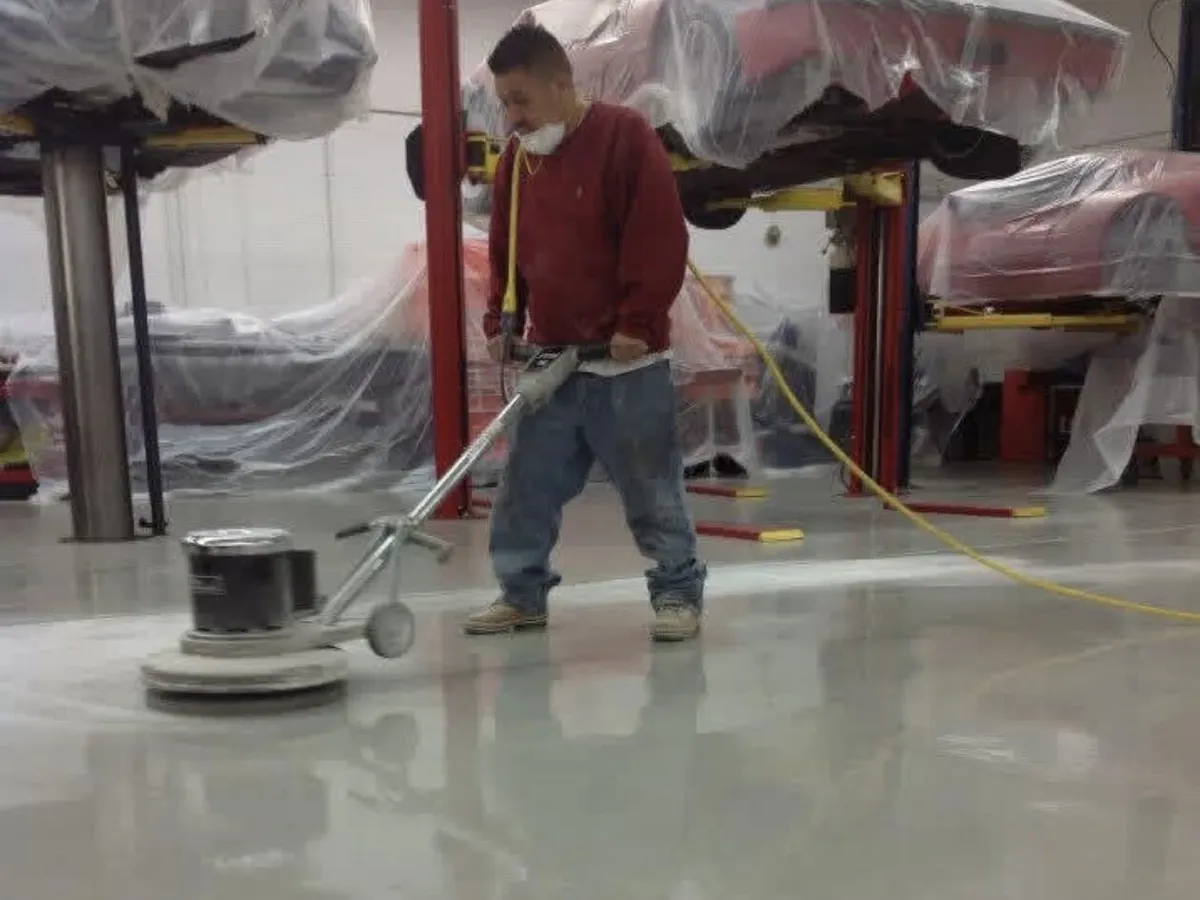 Crew member burnishing the fresh clear coat over the flake floor between the service lifts