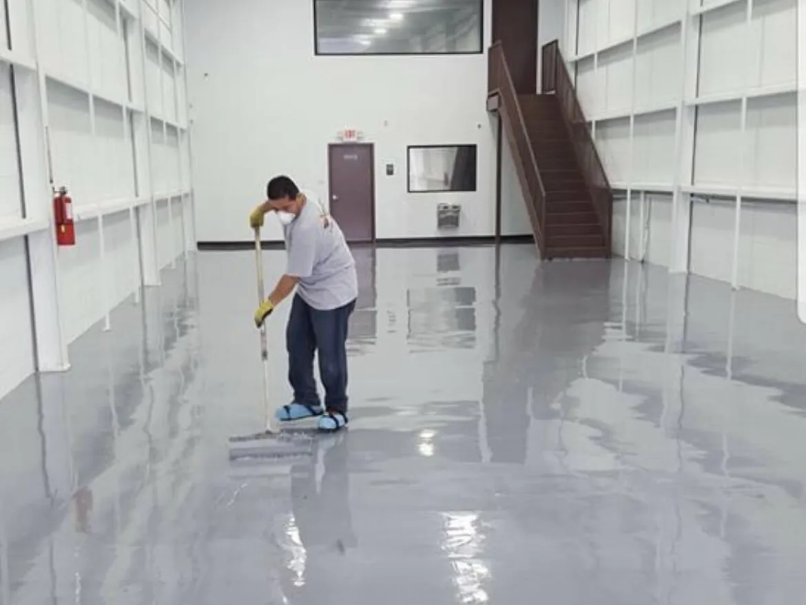 Crew member rolling the final coat on a gray hangar floor