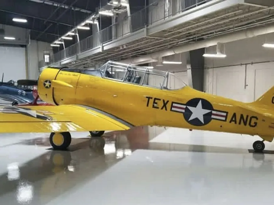 Yellow trainer aircraft parked on the high-gloss white hangar floor at the Lone Star Flight Museum