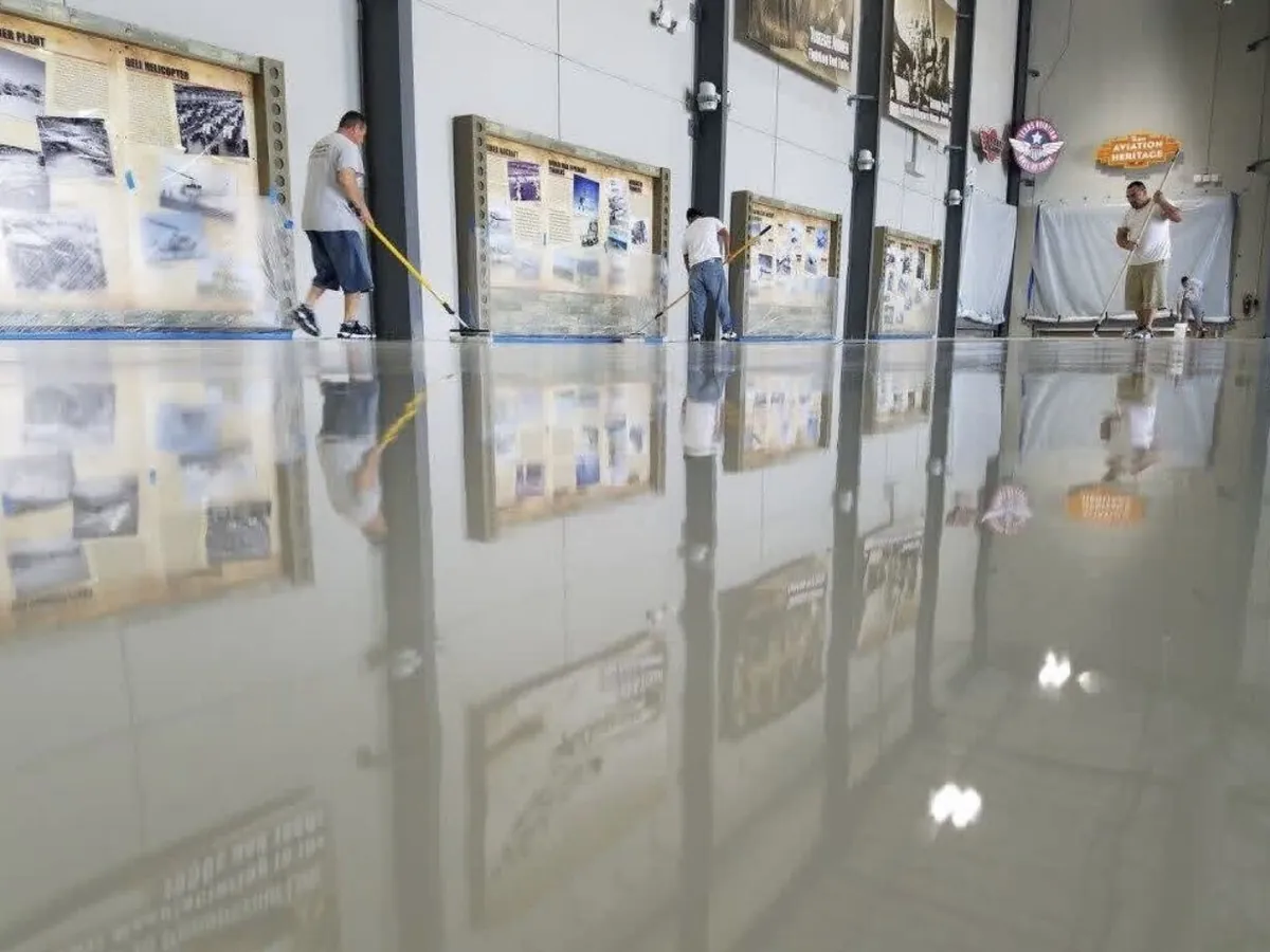 Crew squeegeeing the final clear coat across the hangar floor, the wall displays reflected in it