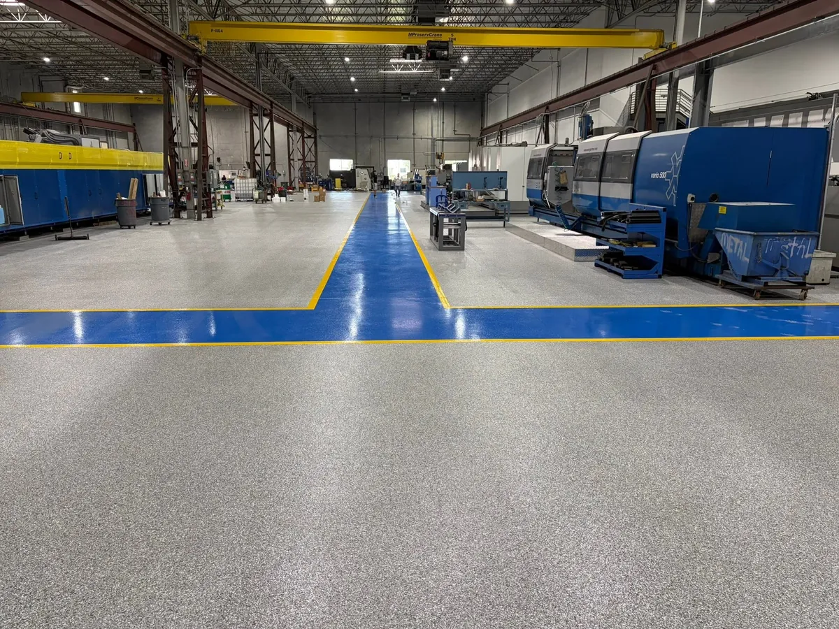 Blue coated walkway with yellow edge lines across a gray flake manufacturing floor